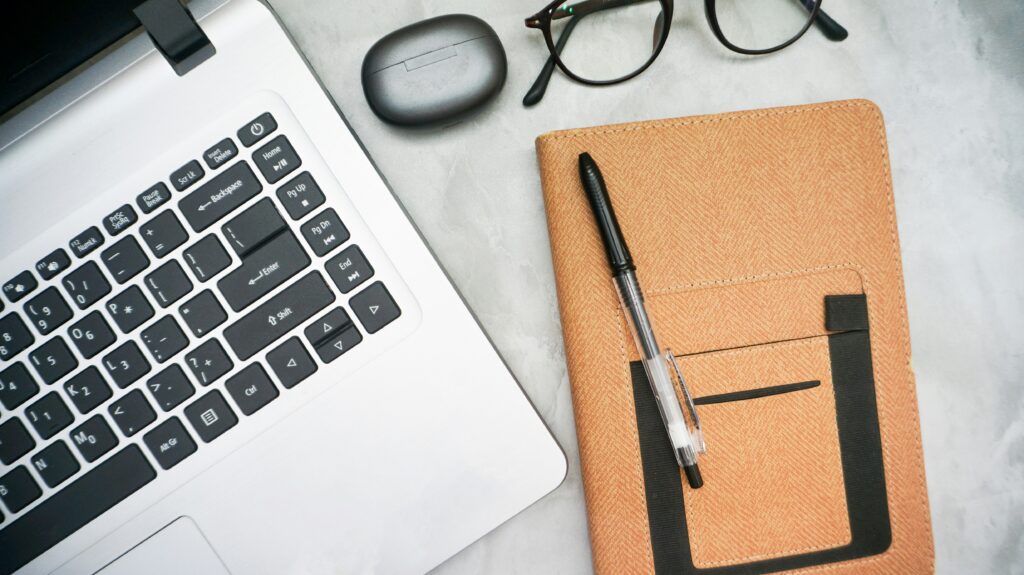 close up of a laptop and notebook with glasses on a desk