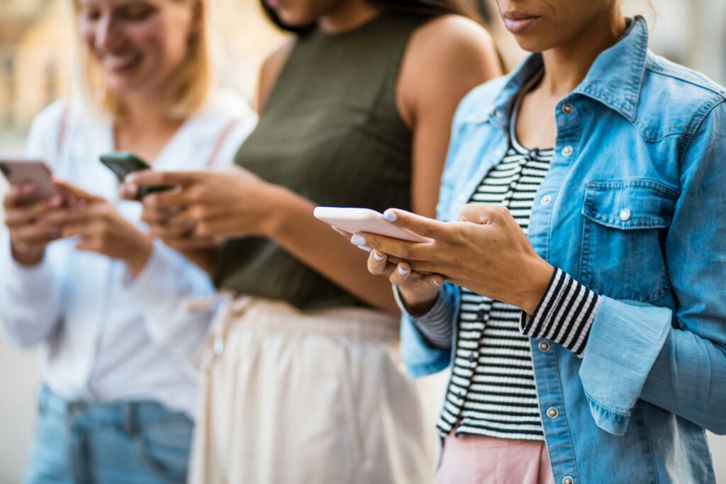 group of young women on their mobile phones stand next to each other
