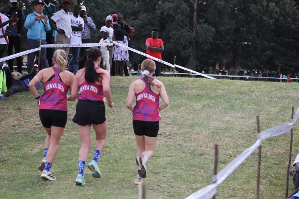 Three female runners in pink tops racing on a grassy outdoor field